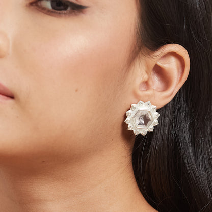 A close-up of a person's ear wearing a silver floral stud earring with a translucent pink hexagonal gemstone centerpiece.