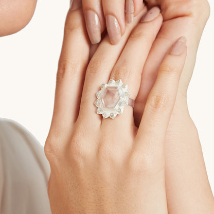 Close-up of a person's hands wearing a silver statement ring featuring a large hexagonal rose quartz stone surrounded by a textured floral halo.