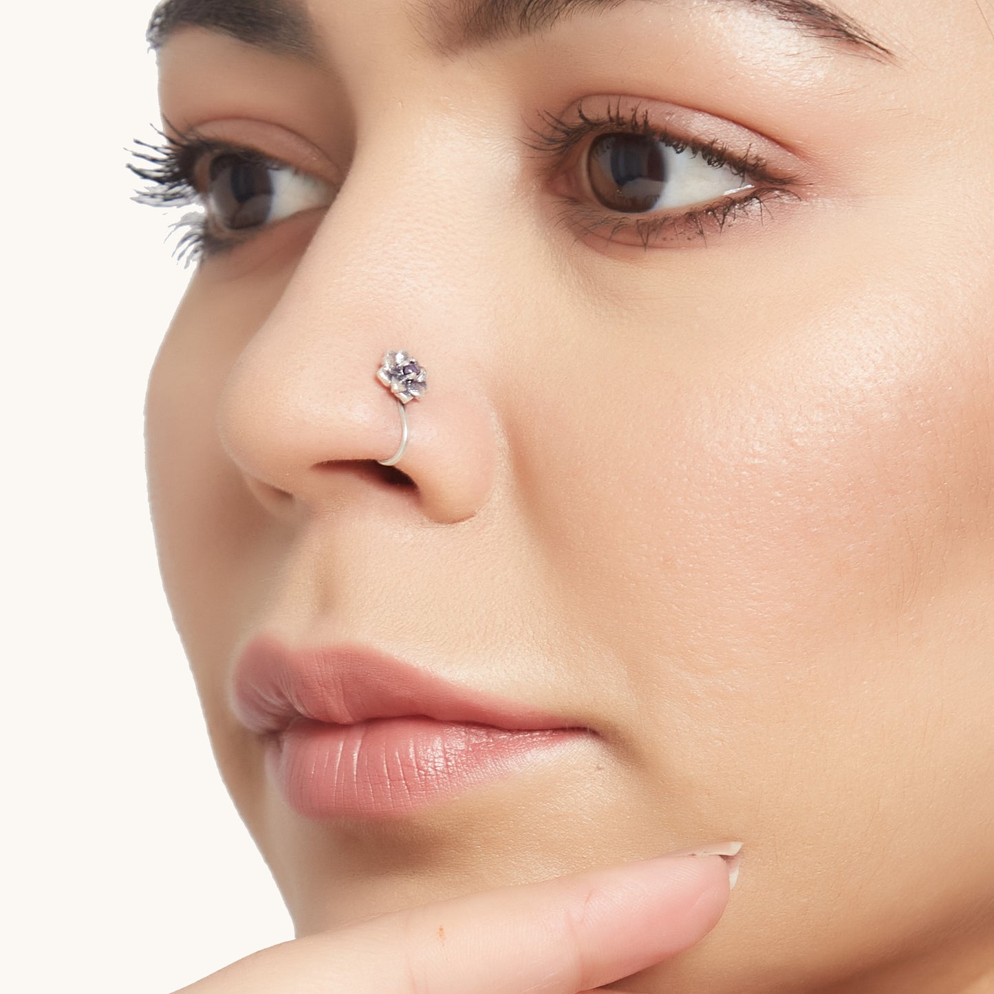 A close-up profile shot of a model wearing a decorative silver-toned, lotus-shaped clip-on nose ring with a dark, circular center stone.