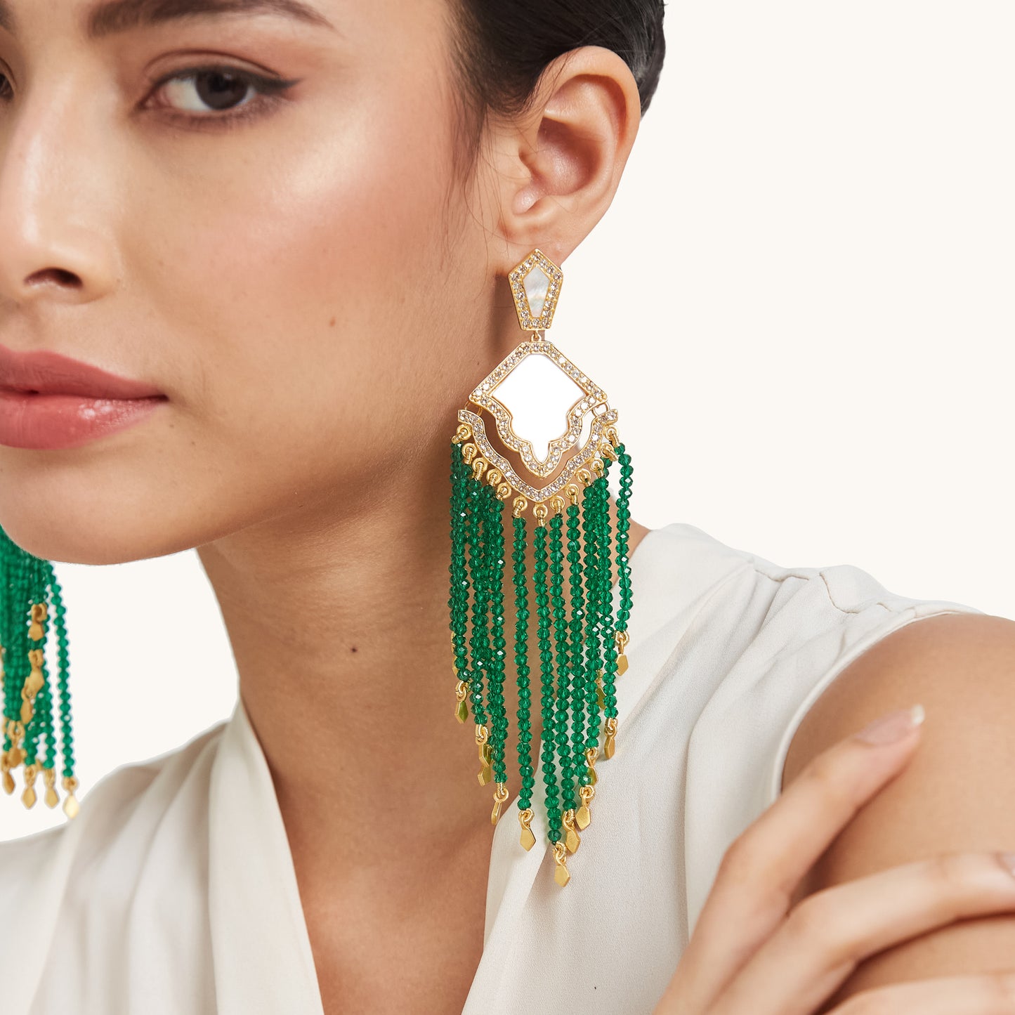 Close-up of a model wearing a long, luxurious shoulder-dusting earring featuring green  beaded tassels and a mother of pearl top.