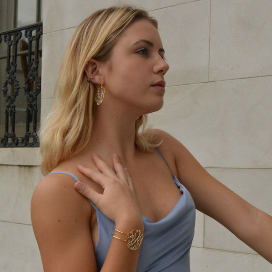 Profile shot of a person showcasing a mixed-metal open-work bangle with a delicate web-like design, styled for a formal occasion.