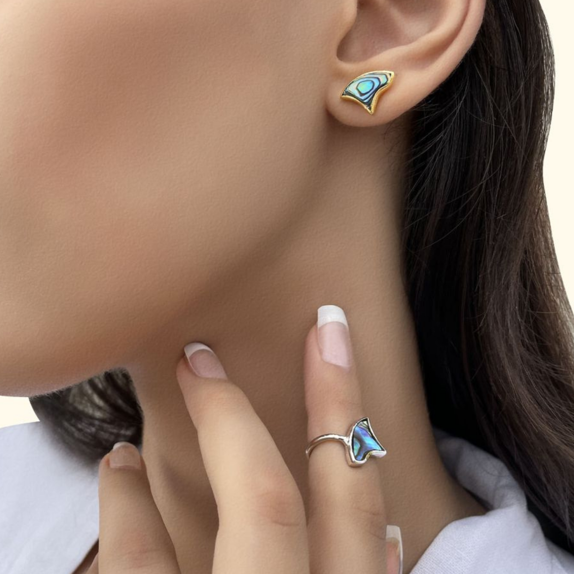 A model posing with her hand near her neck to highlight a dainty silver band ring with a unique, multi-colored shell focal point.