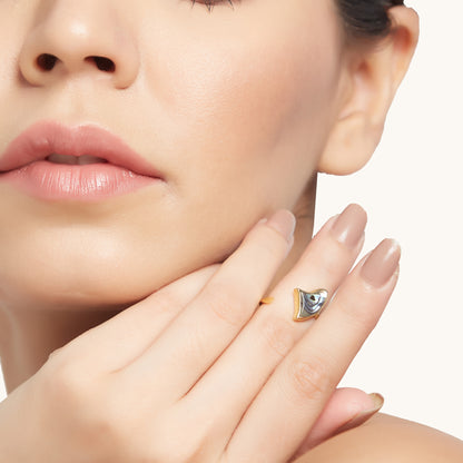 A model posing with her hand near her chin to highlight a dainty gold band ring with a unique, multi-colored shell focal point.
