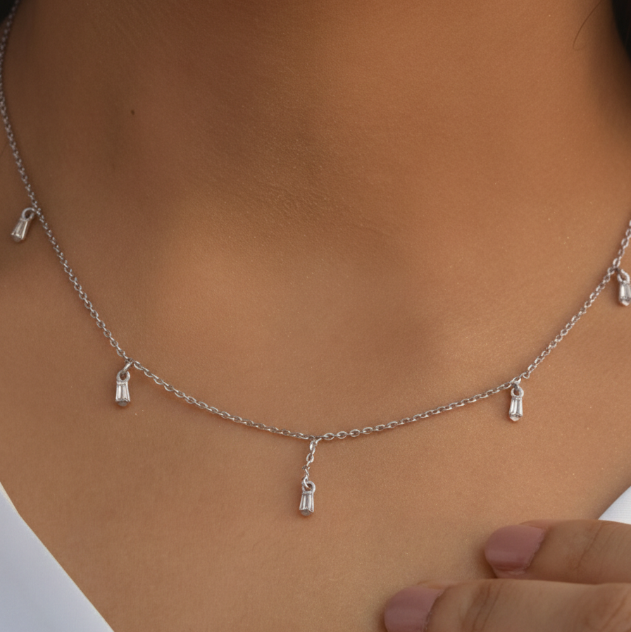 A person wearing a dainty silver-plated chain necklace with small, evenly placed metallic stations that provide a subtle, elegant shimmer.