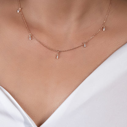 Close-up portrait of a person wearing a refined rose gold necklace, highlighting the graceful way the delicate chain and petite stones drape across the collarbone.