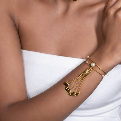 A close-up view of a model's arm wearing an elegant gold cuff bracelet adorned with delicate pearls and a sweeping, fan-like metal accent.
