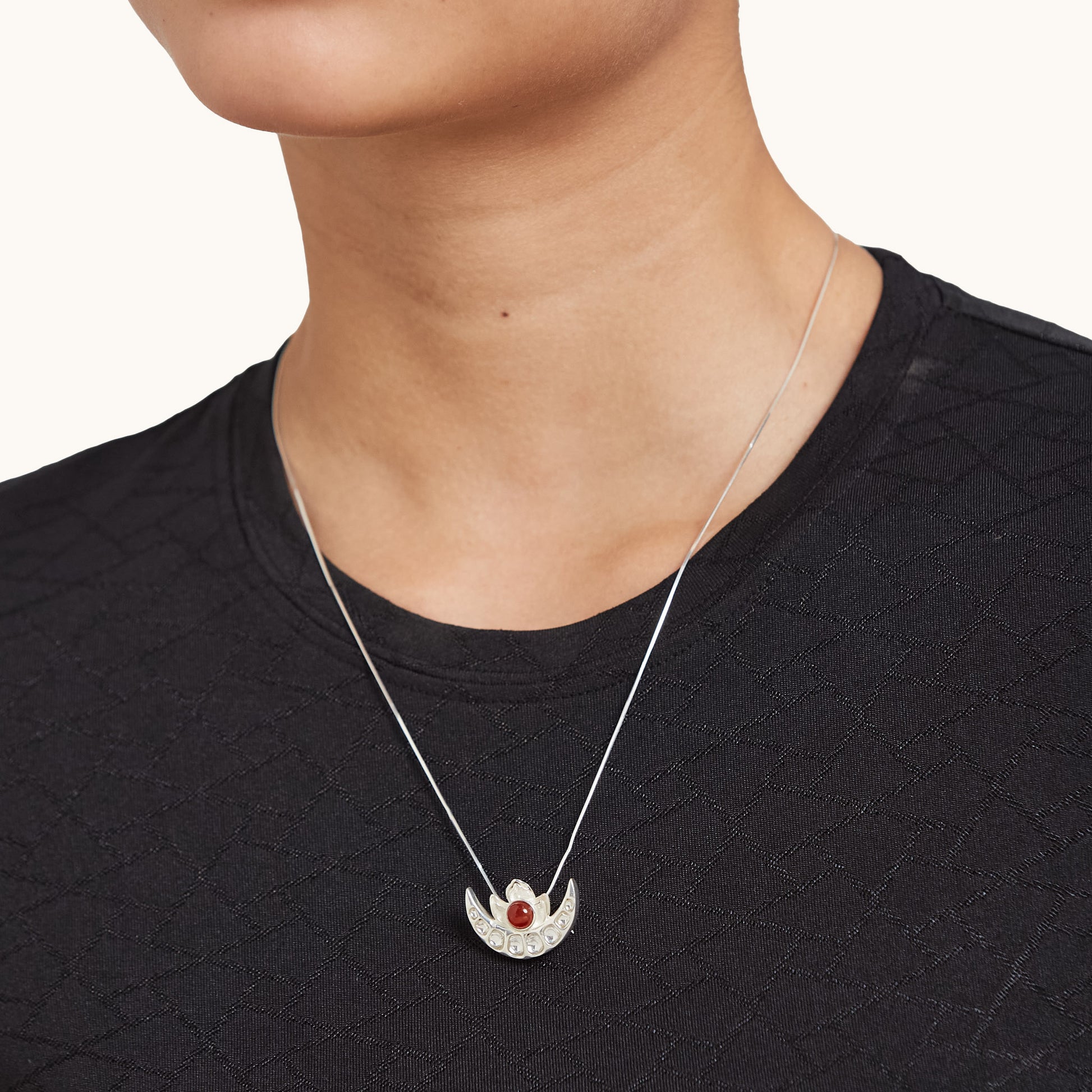 A model wearing a delicate sterling silver half-moon pendant necklace with a red gemstone, styled with a black top.