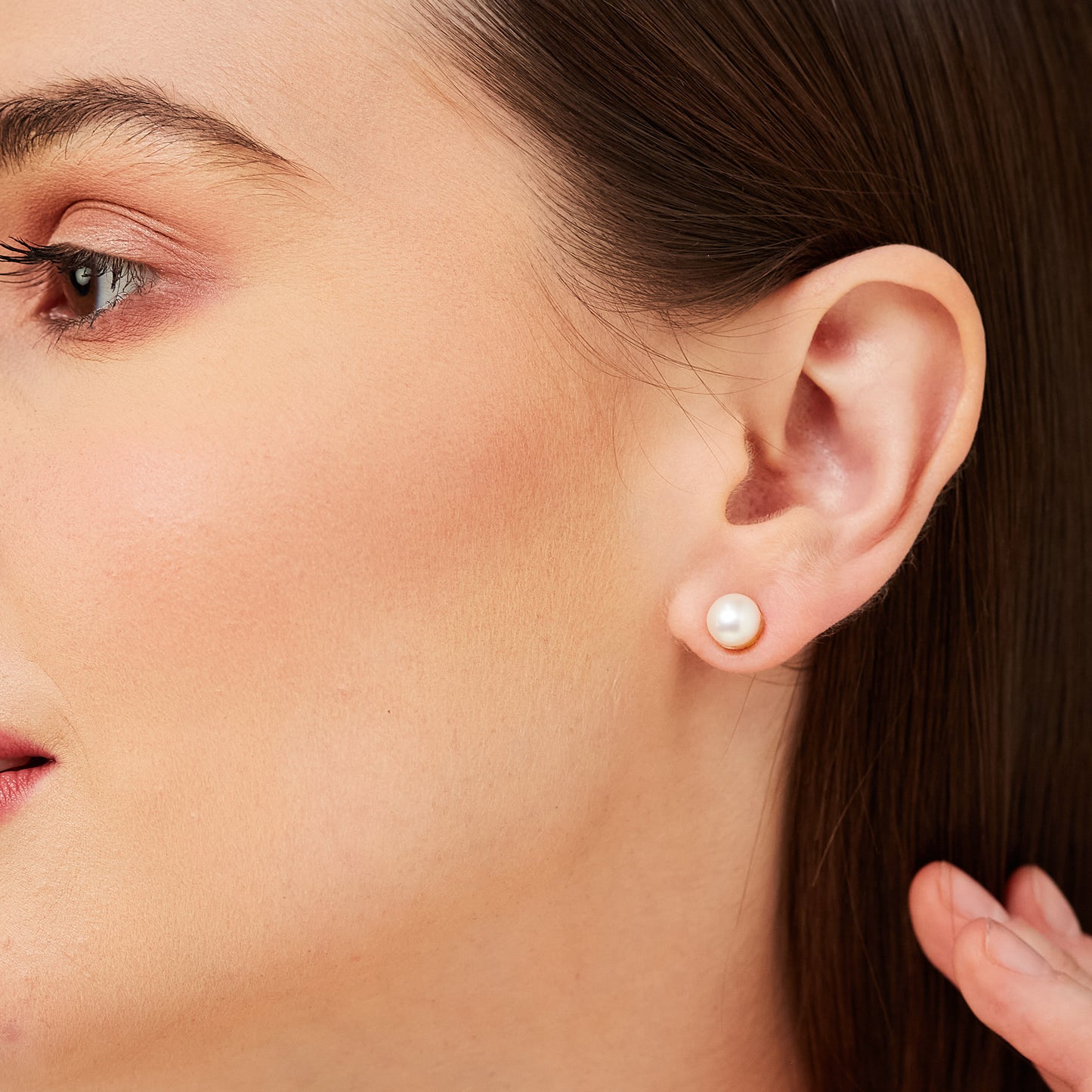 A portrait of a woman wearing only the pearl stud component of the earring for a classic, minimalist jewelry style.