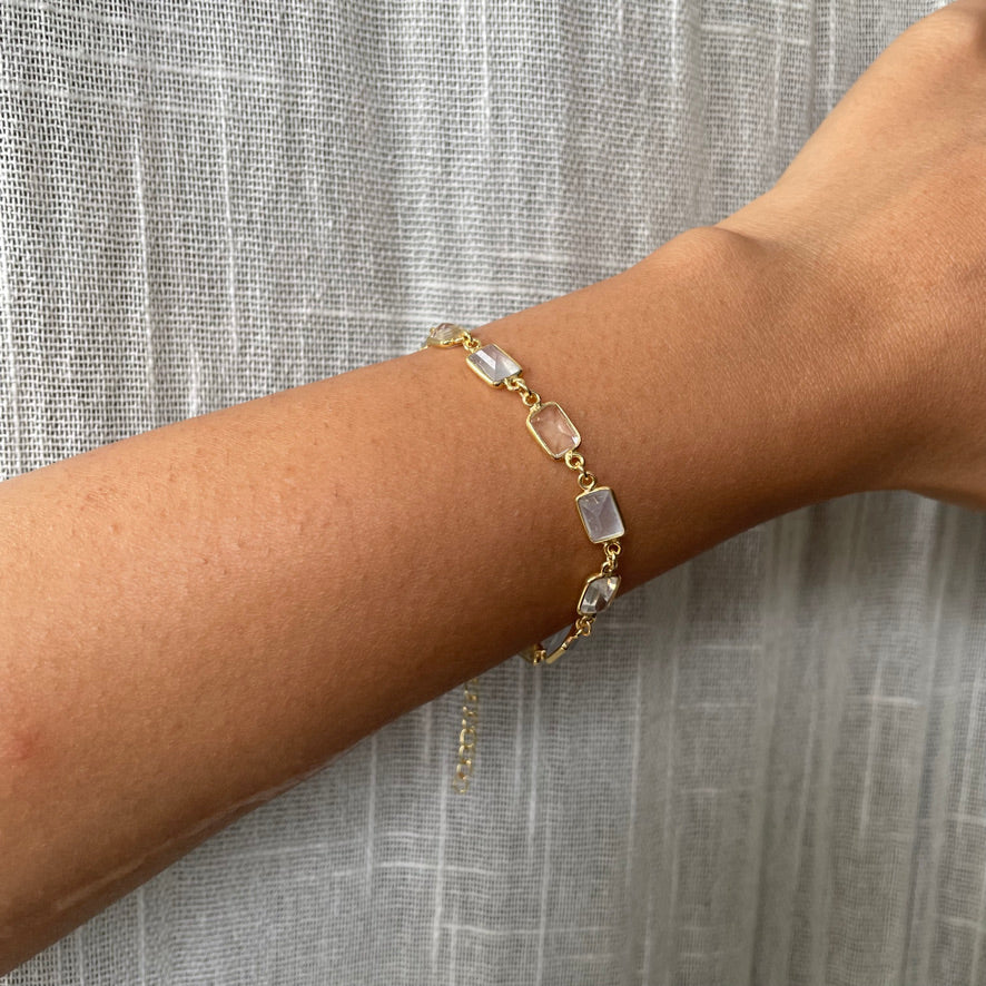 Wrist wearing an elegant gold-plated link bracelet with alternating rectangular pastel and clear stone accents.