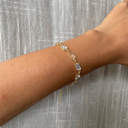 Wrist wearing an elegant gold-plated link bracelet with alternating rectangular pastel and clear stone accents.