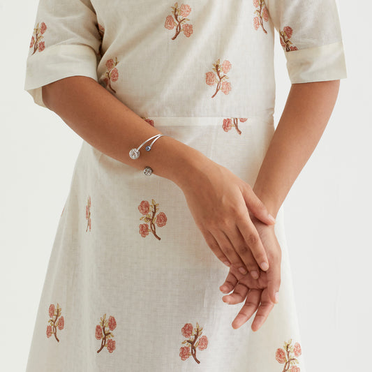 Side profile of a person, showcasing an open-design bracelet with detailed, hollow metal spheres and a pearl accent worn on the wrist.