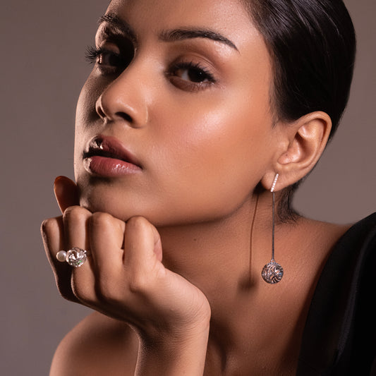Model wearing silver ocean-inspired statement earrings with blue gemstones and a removable stud, styled with a high-neck dark top.