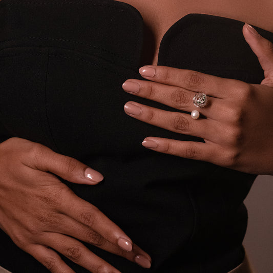 A person wearing an elegant silver-toned ring with a delicate pearl, capturing the soft, natural glow of the piece against the skin for a timeless, sophisticated look.