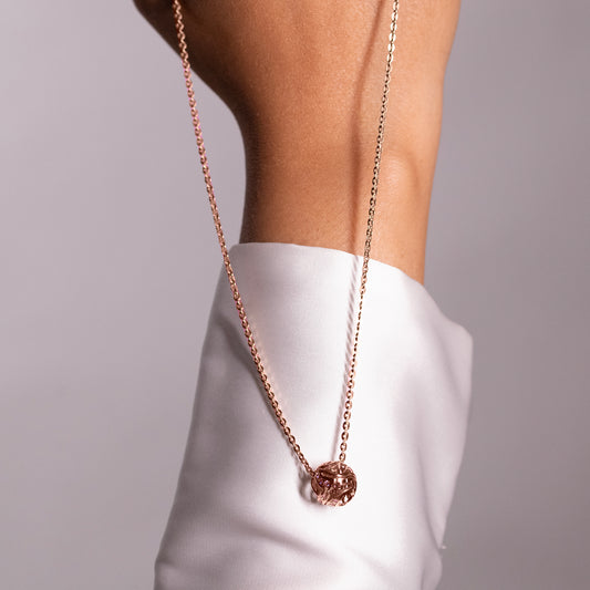 Close-up portrait of a person wearing an organic, fluid-shaped brass pendant, showcasing its polished, reflective surface and contemporary aesthetic.