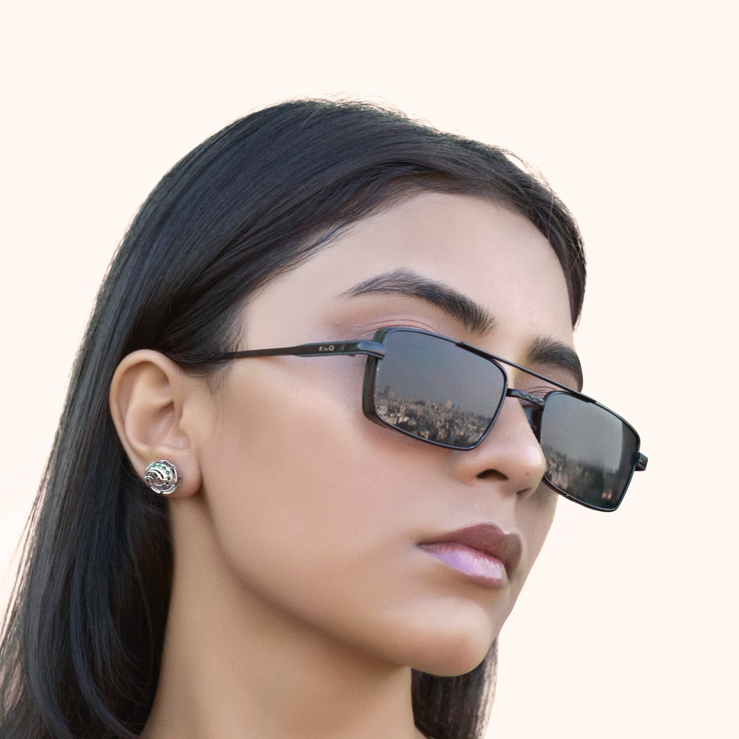 Close-up of a model wearing silver-toned geometric stud earrings with a nautical lattice design and vibrant teal and blue gemstones.
