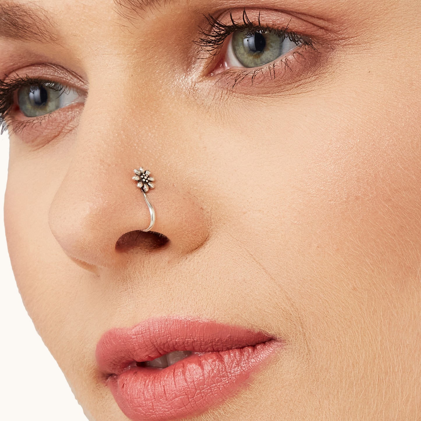 A close-up profile view of a model wearing an intricate, silver-toned, flower-shaped non-piercing nose clip-on.