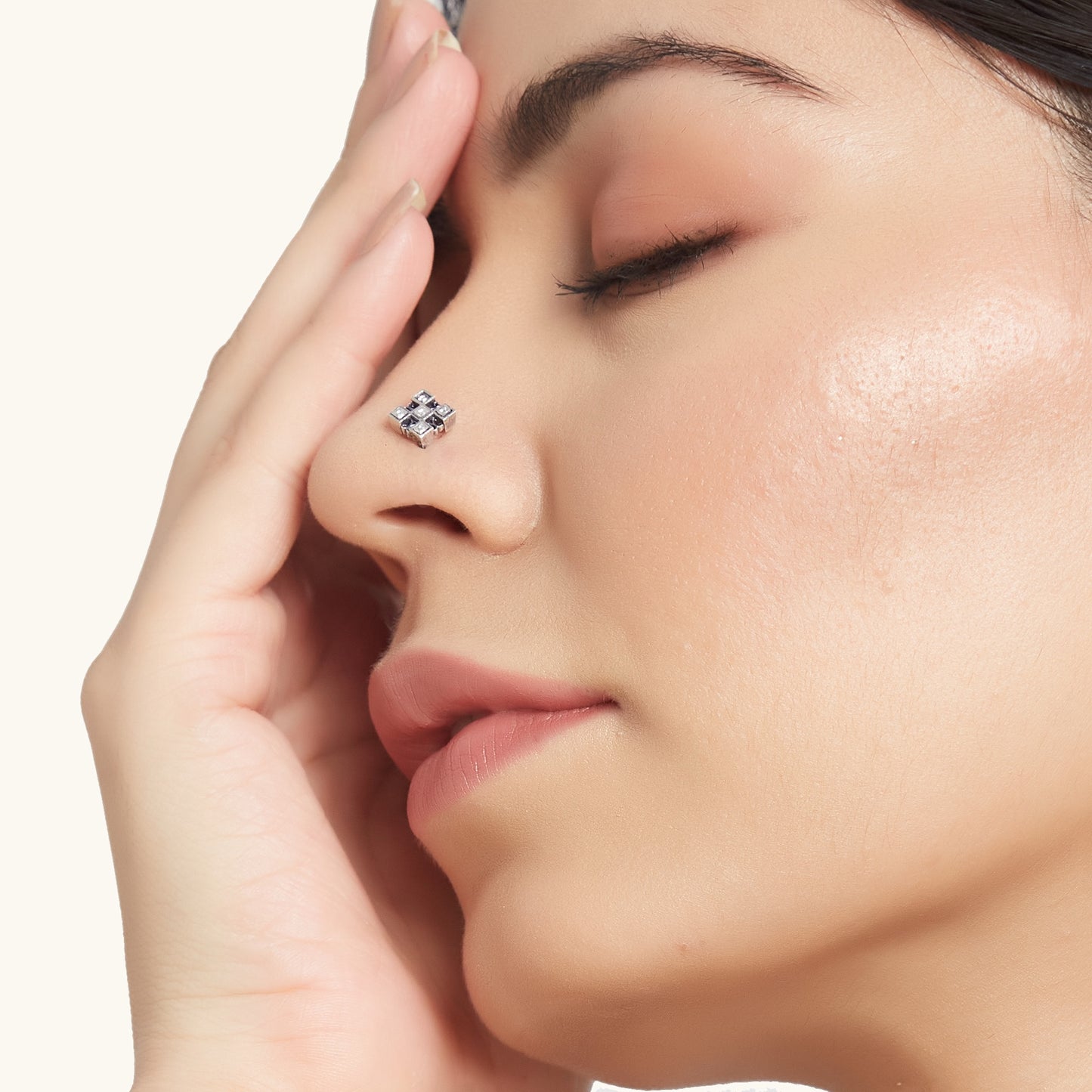 Close-up profile of a model wearing a geometric diamond-shaped silver nose pin with inlaid stones, with her hand gently resting near her face.