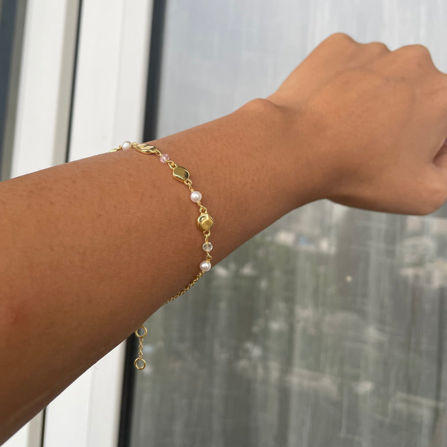 A model wearing a gold-tone chain bracelet featuring delicate pearls and small pebble charms on their wrist.