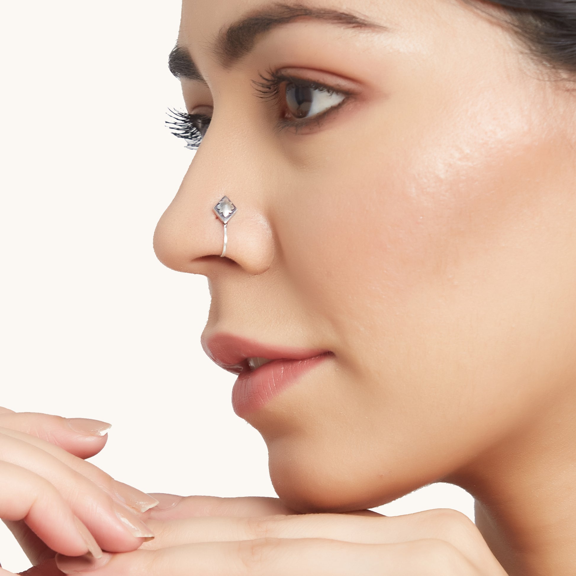 A side-profile view of a model wearing a diamond-shaped silver clip on with a central floral motif positioned in their nostril.