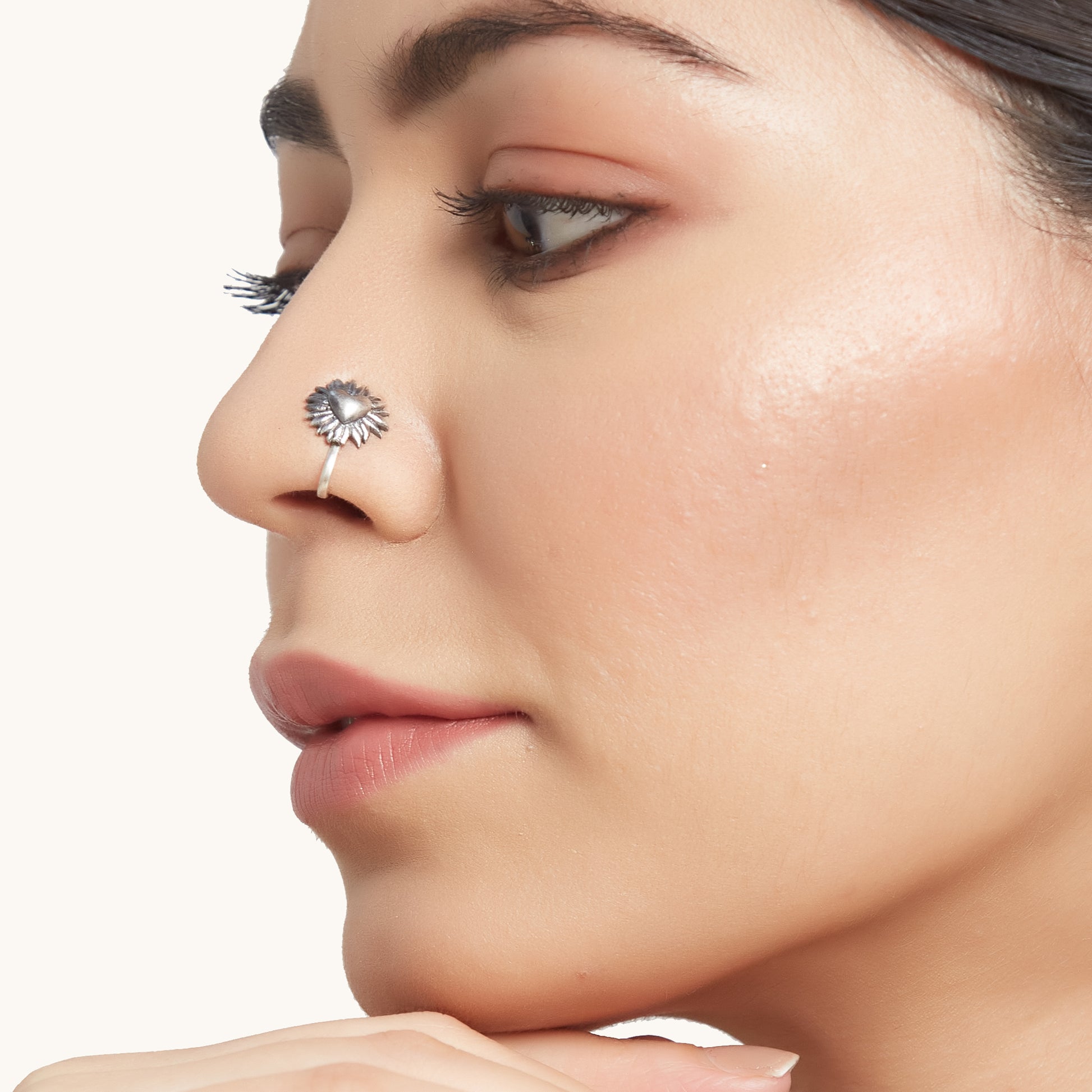 Side-profile portrait of a model wearing an elegant botanical-inspired silver facial adornment on the nostril
