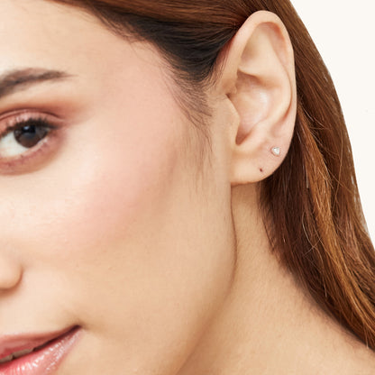 Tiny gold trillion-cut sparkling studs shown as a pair, perfect for second or third lobe piercings.