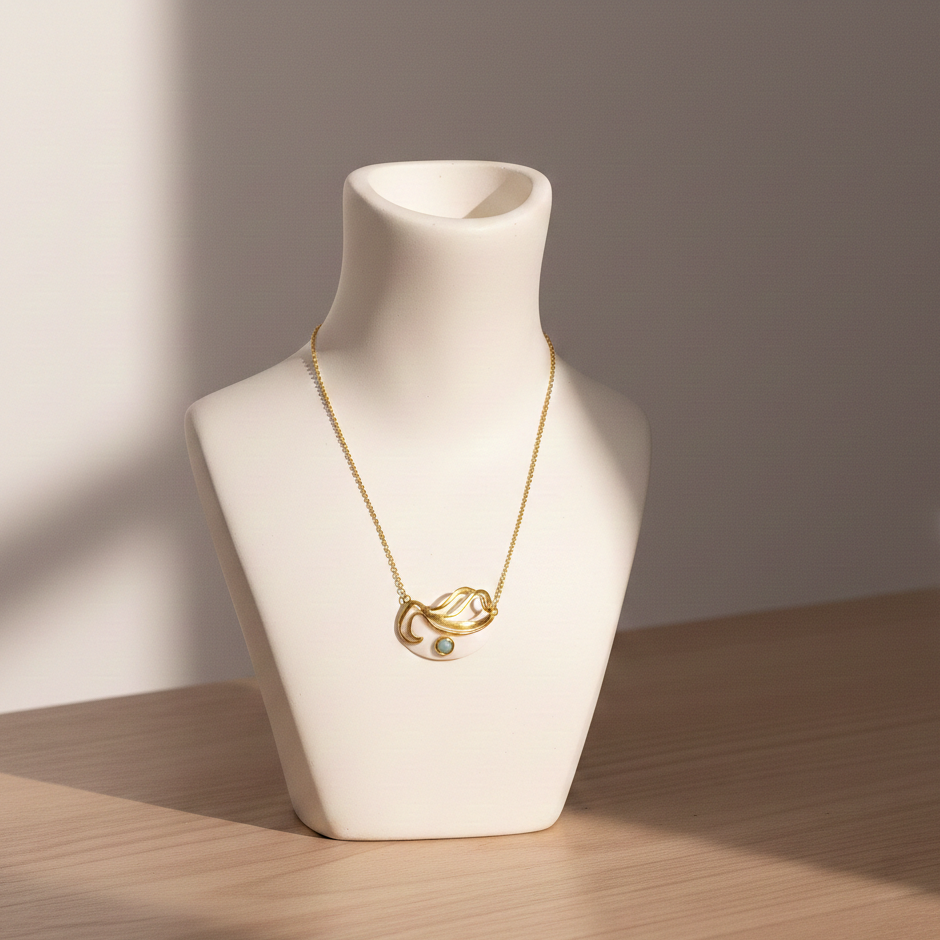 Mystic Turquoise Necklace featuring a delicate gold chain with an abstract wave pendant and a small turquoise stone, displayed on a white bust stand in soft natural light.