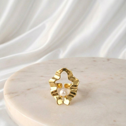 Pearl Drop Ring featuring a sculptural open gold design with a single pearl detail, displayed on a round marble pedestal against soft white draped fabric.