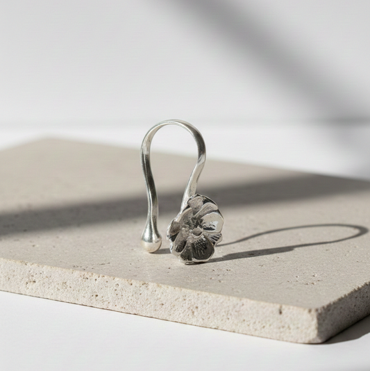 Silver Peony Nose Clip featuring a sculpted floral design with curved hook style, displayed on a neutral stone surface in soft natural light.