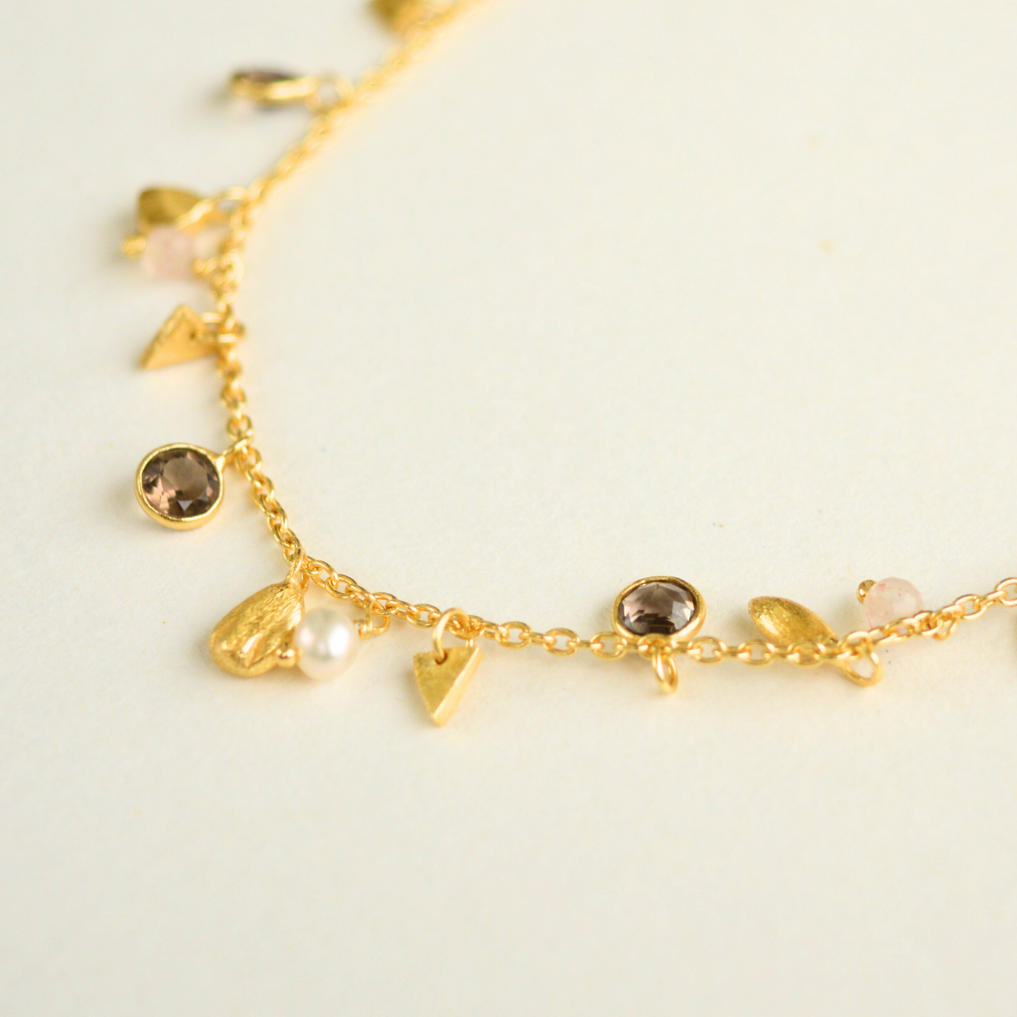 A close-up showing the texture and arrangement of dangling pebble charms, small white pearls, and clear quartz beads on a fine gold-plated chain.