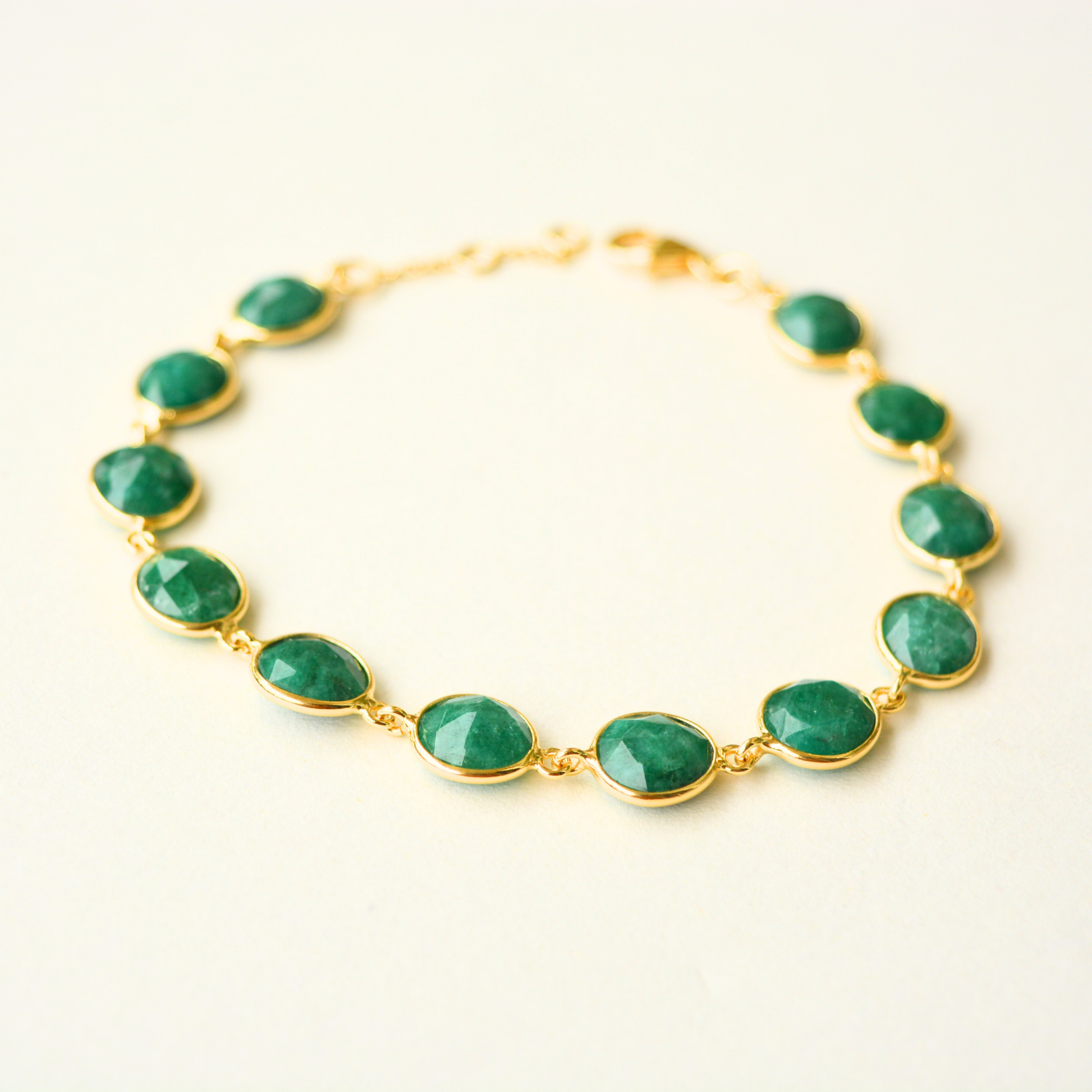 A delicate gold-plated silver chain bracelet featuring oval-cut green emerald stones and an adjustable sliding clasp, centered on a white background.