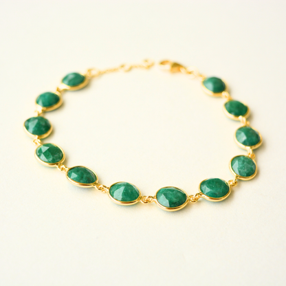 A delicate gold-plated silver chain bracelet featuring oval-cut green emerald stones and an adjustable sliding clasp, centered on a white background.