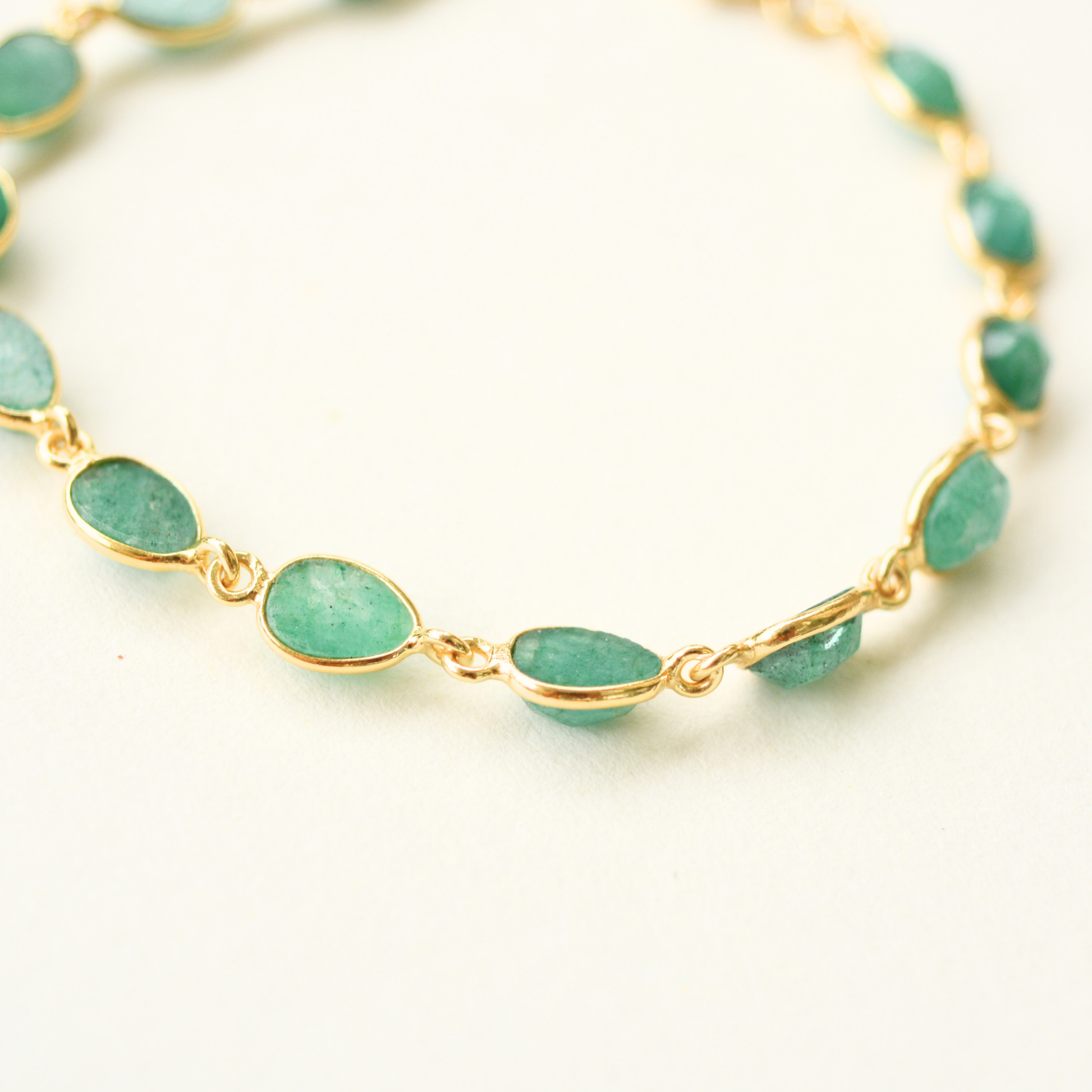 A close-up view showing the bezel-set, oval-cut green beryl stones connected by gold-plated silver links.
