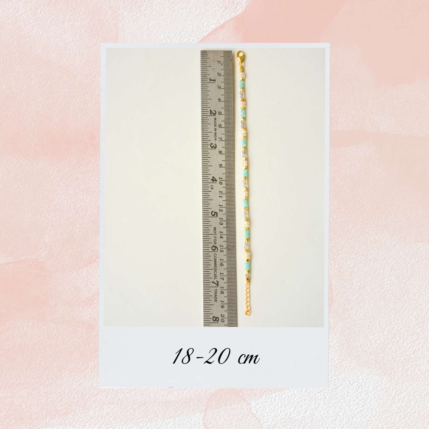 A light blue and pearl beaded chain bracelet displayed against a metal ruler, showing an adjustable length of 18 to 20 cm.