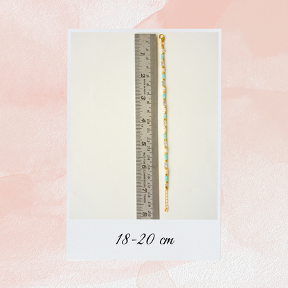 A light blue and pearl beaded chain bracelet displayed against a metal ruler, showing an adjustable length of 18 to 20 cm.