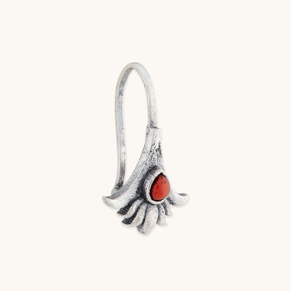 An angled close-up of a handcrafted, antique-finish silver clip-on nose piece with a central, square-cut reddish-orange  gemstone set in a petal-shaped design.