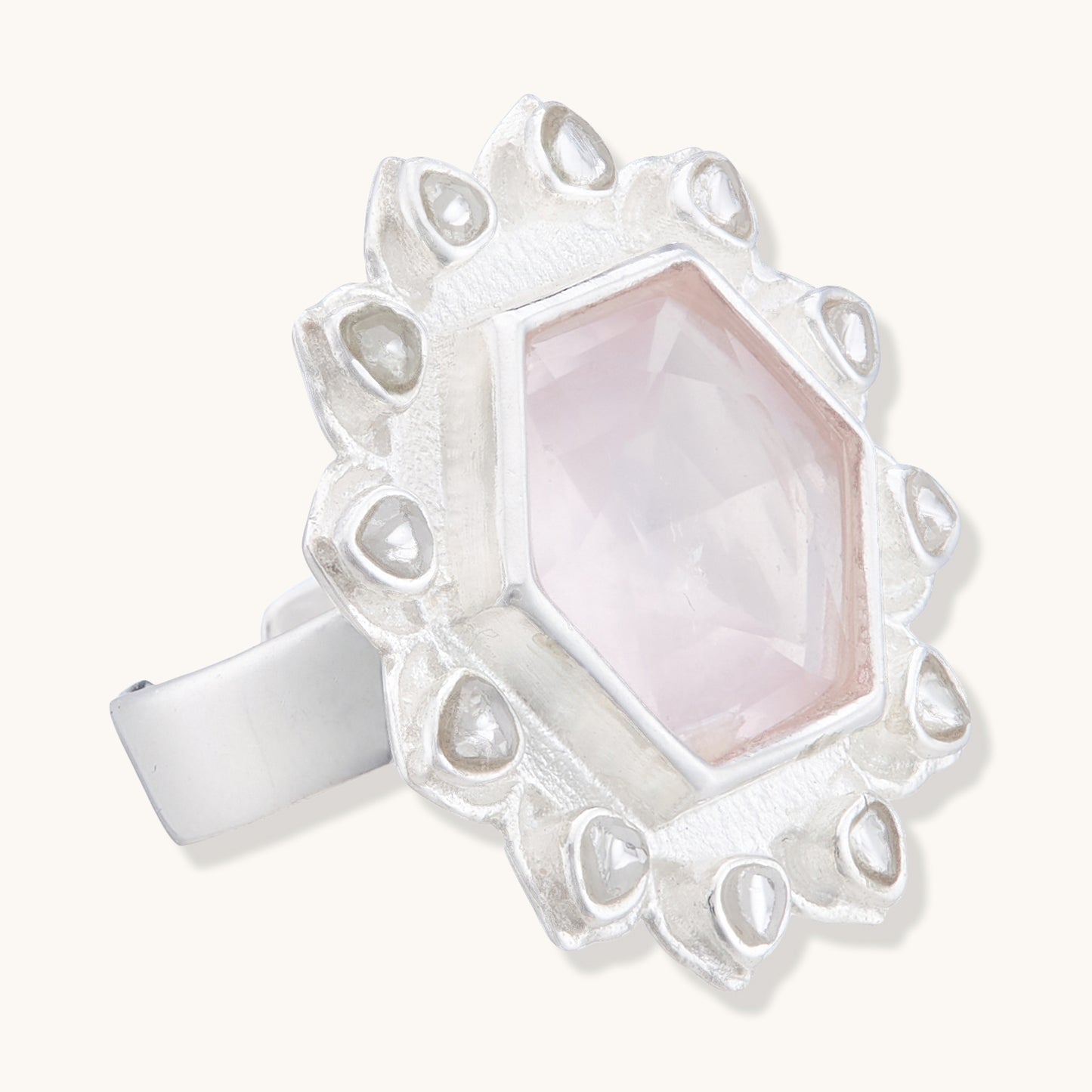 Angled side view of a silver artisan ring displaying the thick band and the raised setting of a pale pink hexagonal stone with a textured sunburst frame.