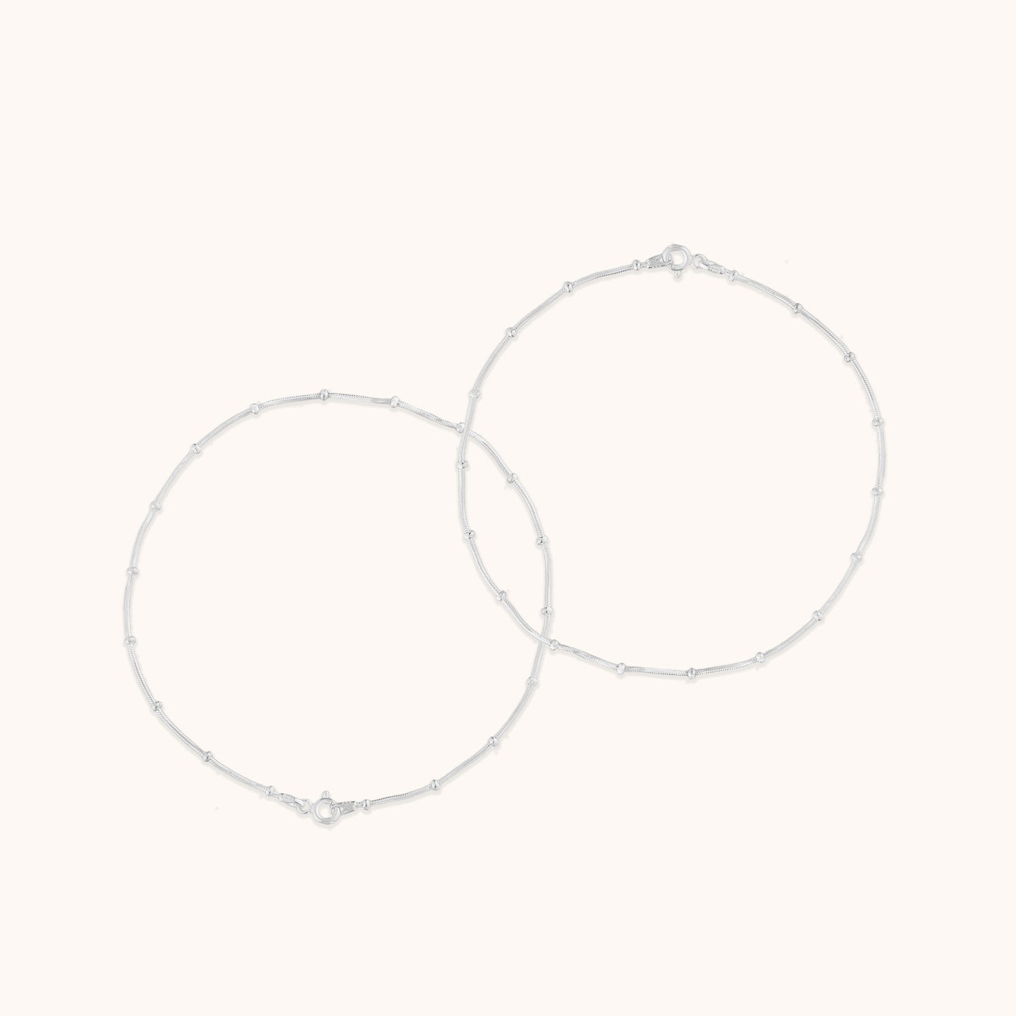 Two thin, minimalist silver chains decorated with small, uniform beads, displayed in a circular arrangement.