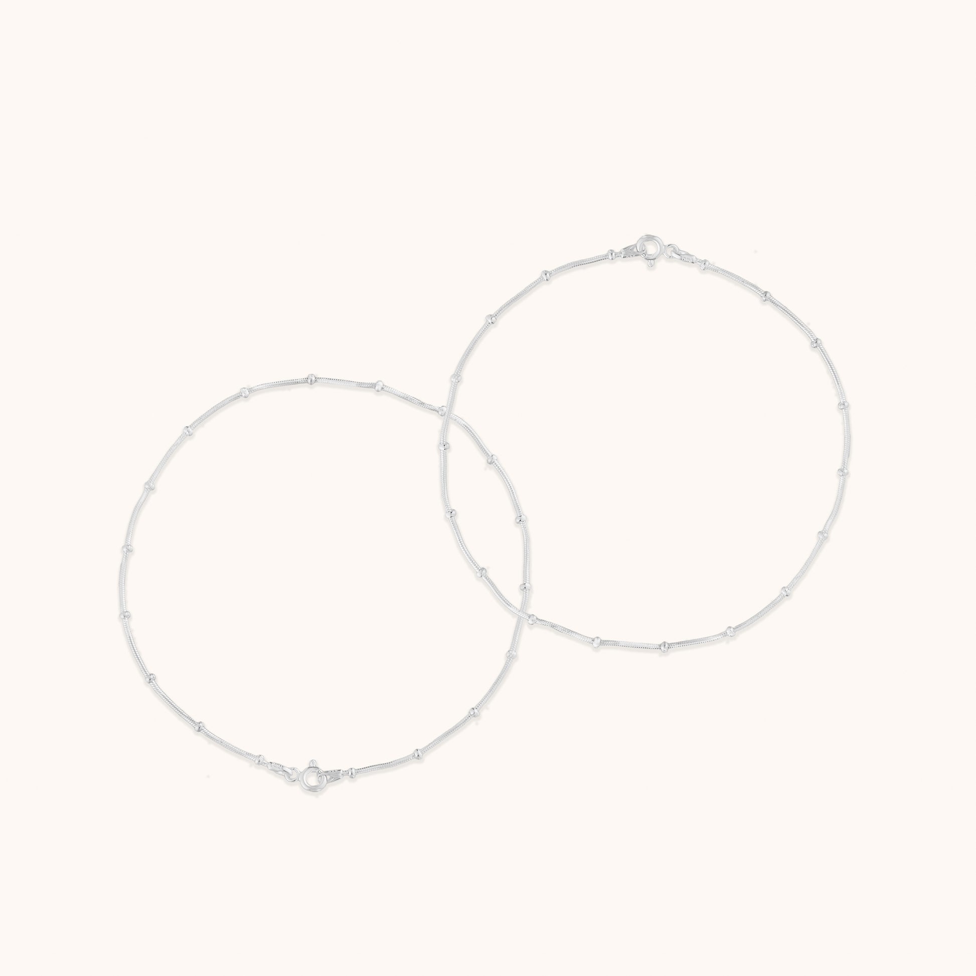 Two thin, minimalist silver chains decorated with small, uniform beads, displayed in a circular arrangement.