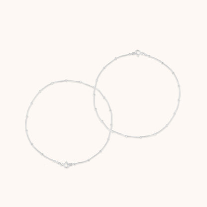 Two thin, minimalist silver chains decorated with small, uniform beads, displayed in a circular arrangement.