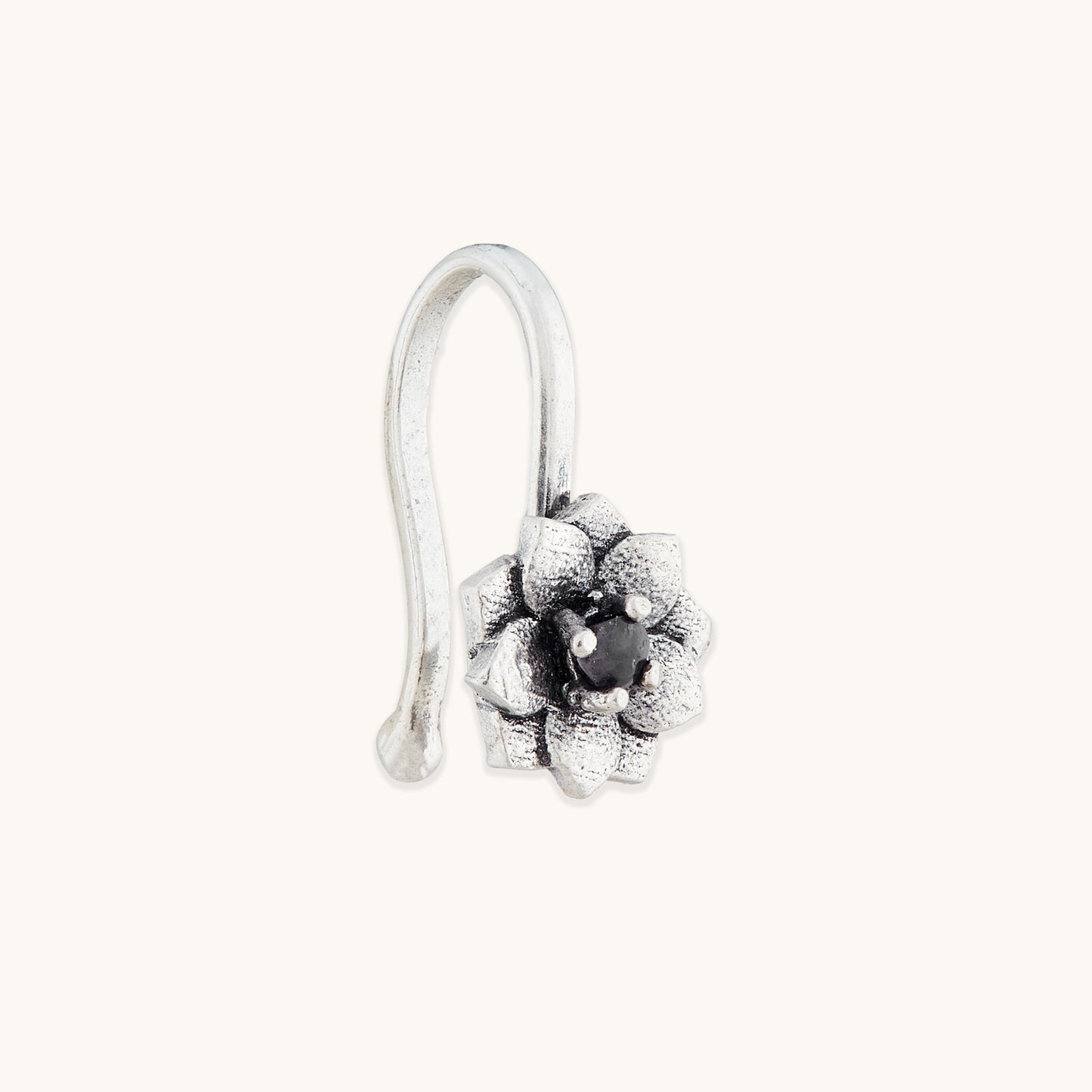 An angled view of an antique-finish silver clip-on nose accessory with an ornate, multi-petaled floral design and a dark central accent.