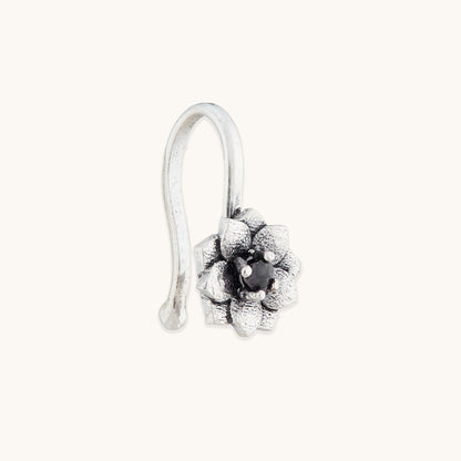 An angled view of an antique-finish silver clip-on nose accessory with an ornate, multi-petaled floral design and a dark central accent.
