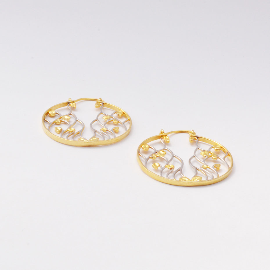 Close-up shot of two-tone circular earrings with a detailed filigree vine pattern on a clean, light background.