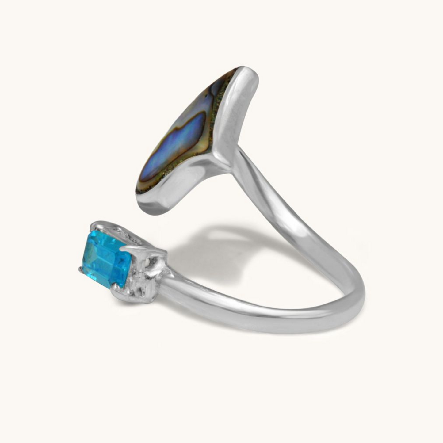 A side-angle studio view of an open-style silver ring, highlighting the placement of the iridescent abalone shell inlay and the rectangular blue gemstone.