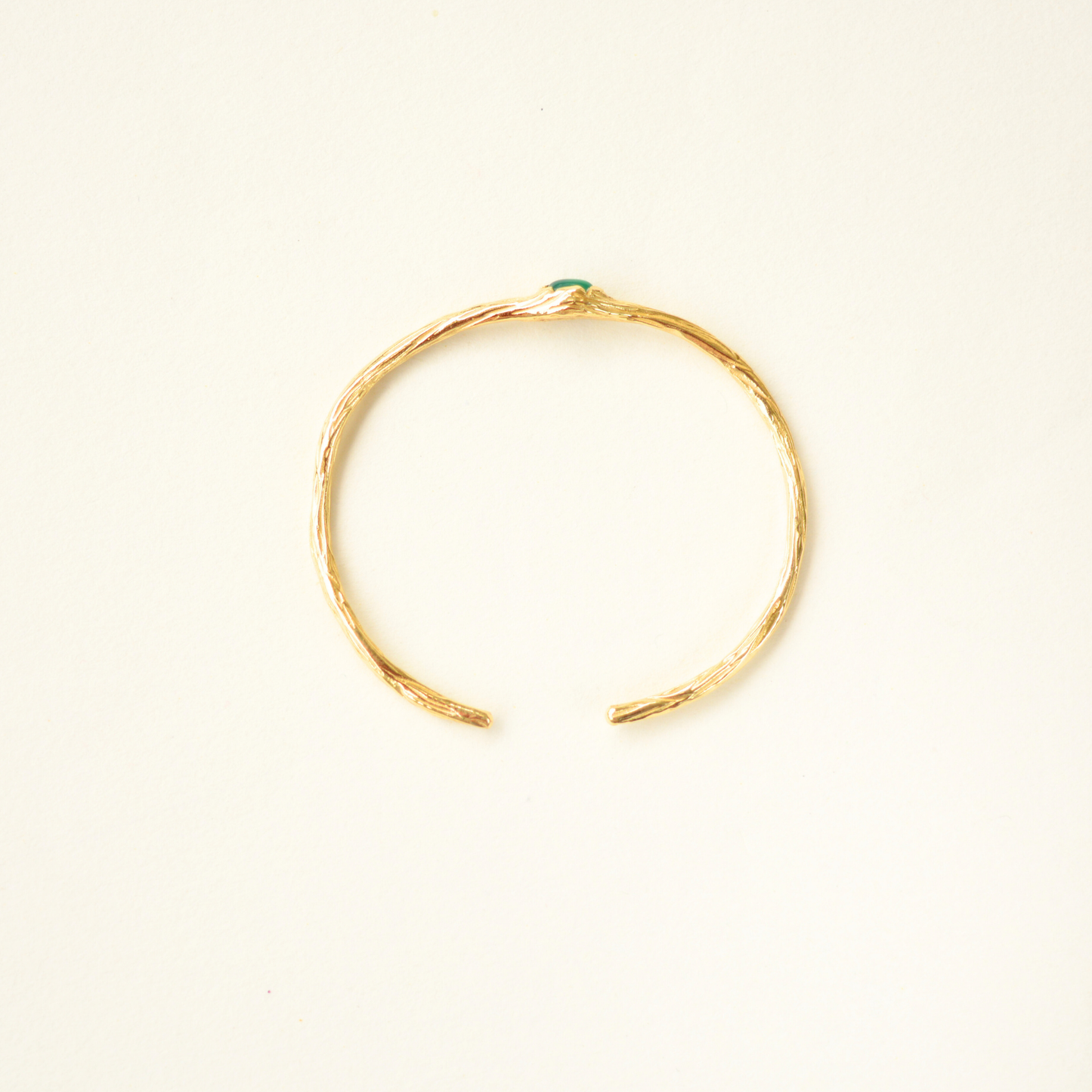 Top-view of a gold-plated cuff bracelet featuring a detailed, organic textured band and a center green stone.