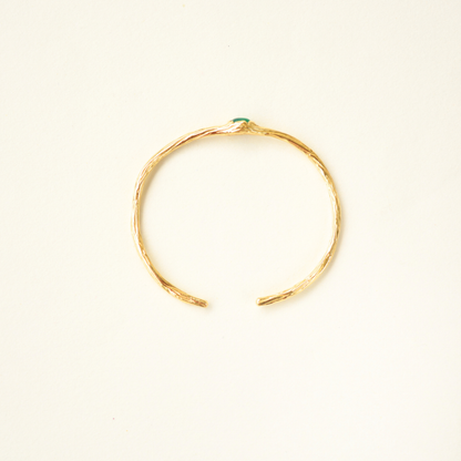 Top-view of a gold-plated cuff bracelet featuring a detailed, organic textured band and a center green stone.