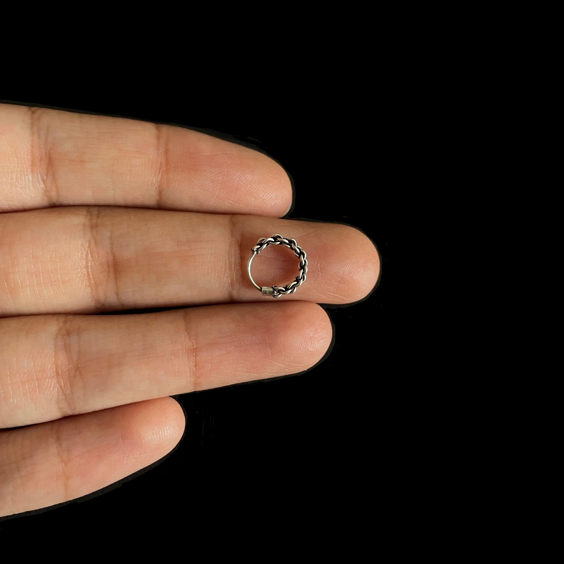 A close-up view of a small, textured silver hoop resting on a person's finger, highlighting the intricate braided metal design.