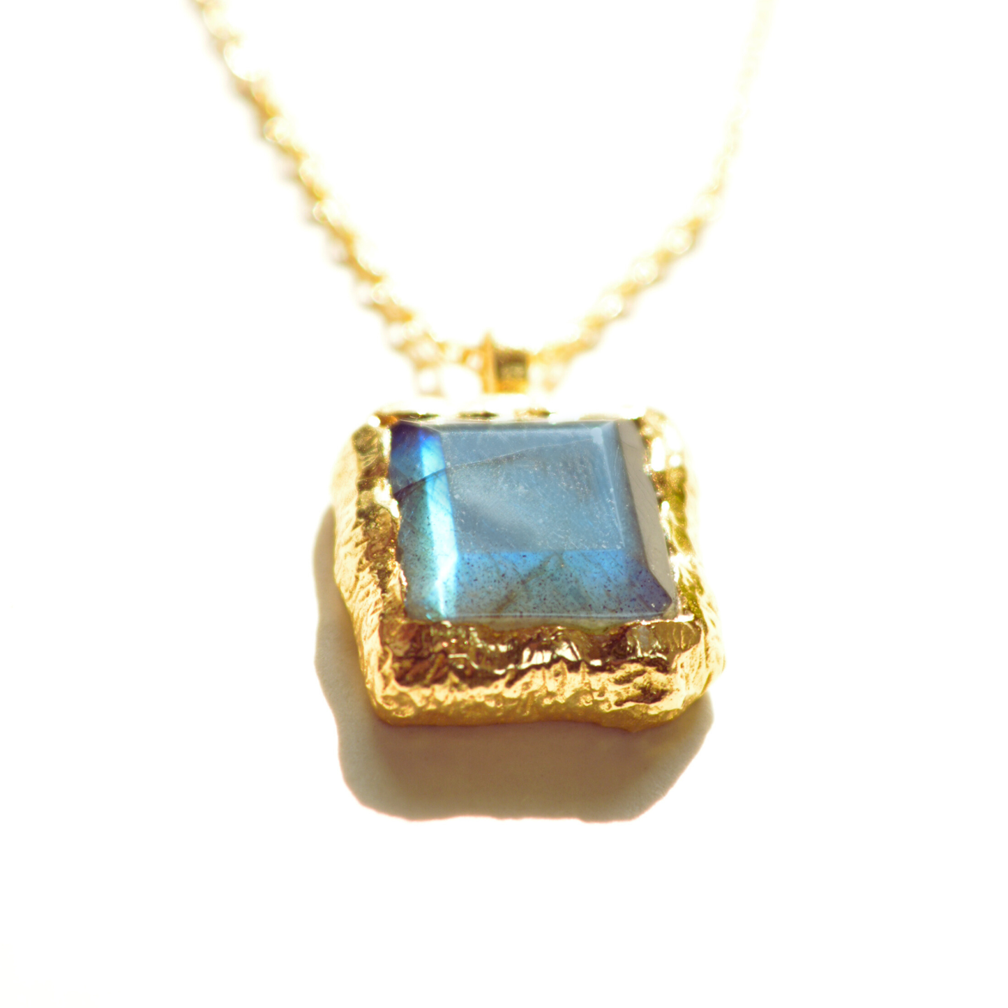 Close-up of a multifaceted labradorite necklace charm displaying iridescent flashes of blue and green, handcrafted in sterling silver.

