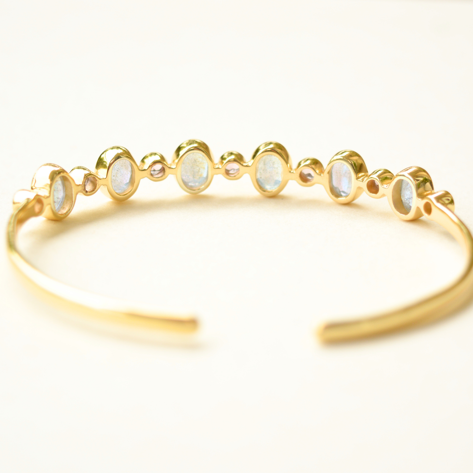 Close-up of a minimalist silver cuff with polished violet and glowing labradorite gemstone terminals, isolated on white.