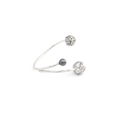 A silver, open-ended bracelet featuring two hollow, filigree-style spheres with  accents and one smooth pearl charm, isolated on a white background.