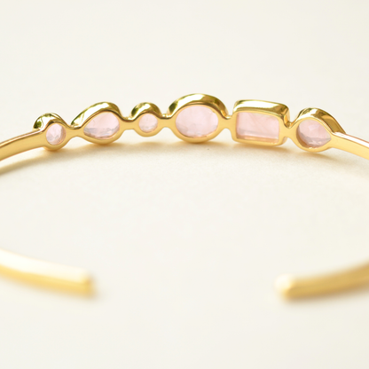 A close-up of a gold cuff bracelet detailing a variety of faceted rose quartz settings.